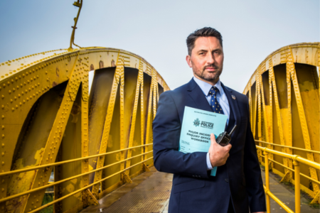 Northumbria Police detective holding papers and a radio facing the camera on a yellow bridge